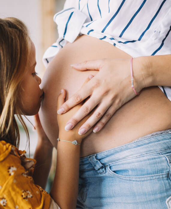 Happy kid girl hugging beautiful pregnant mother's belly